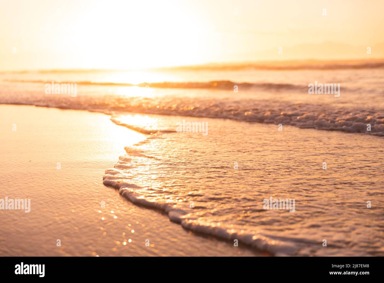 Scenic view of waves splashing at shore and bright sun reflecting on seascape against sky at sunset Stock Photo