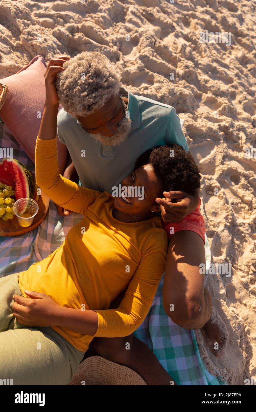 High angle view of happy african american mature woman lying on senior man's lap on sandy beach Stock Photo