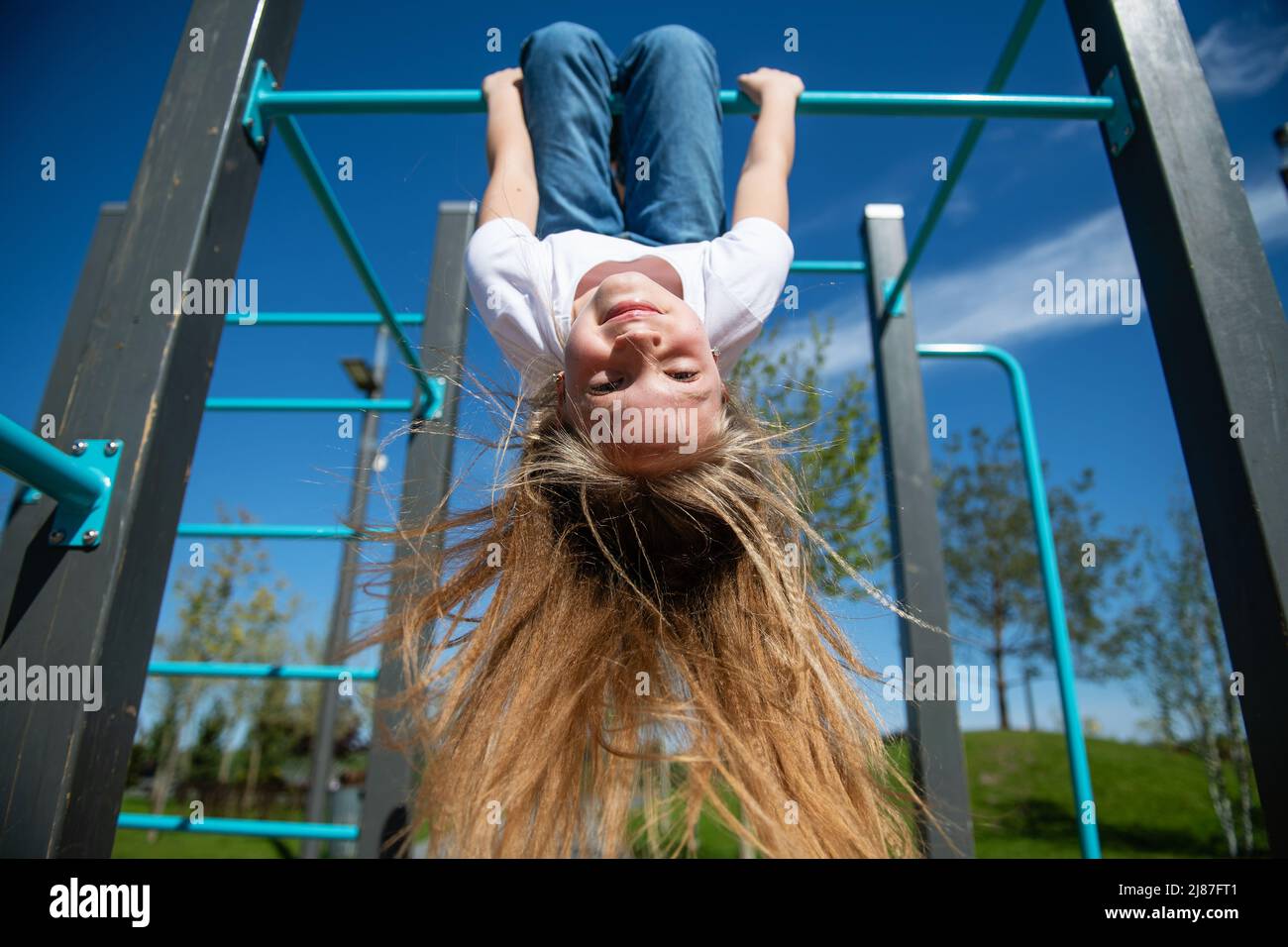 A beautiful teenage girl hanging upside down on the horizontal bar. Hair is blowing in the wind. Bottom view, wide angle. Stock Photo