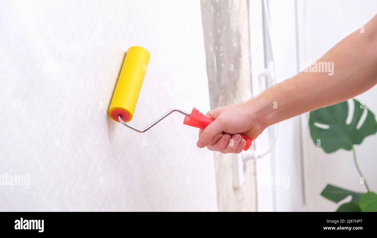 A man rolls out a canvas of white wallpaper with a suture yellow roller