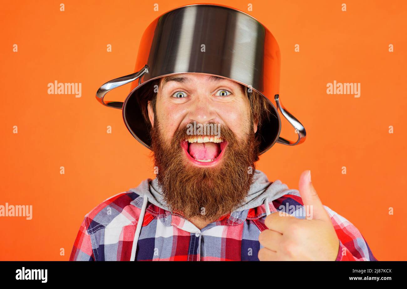 Bearded man with pot on head showing thumb up. Kitchenware. Cooking utensil for food preparation. Stock Photo