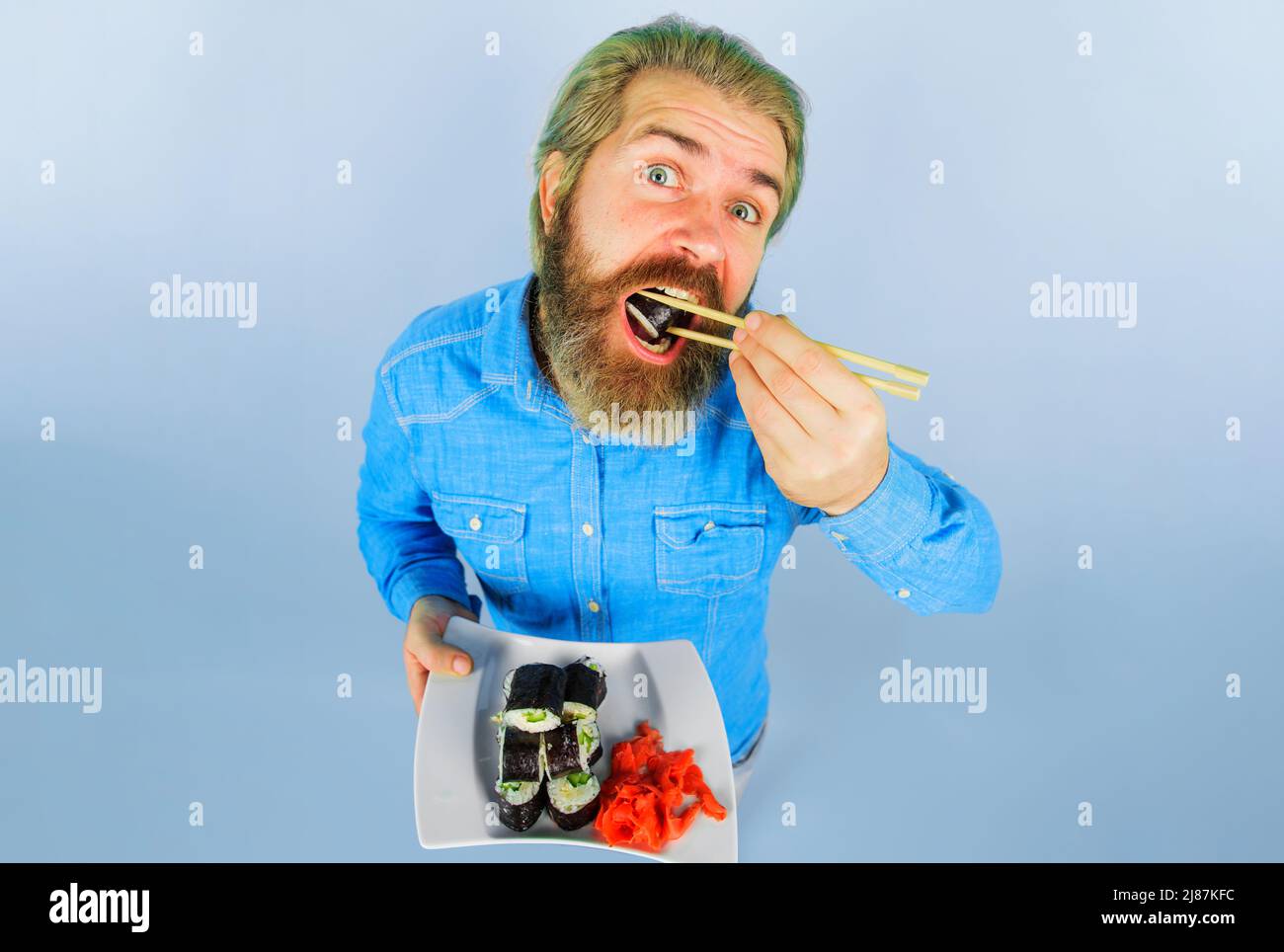 Bearded man eating sushi. Handsome guy with Plate of sushi roll and pickled ginger. Japanese food. Stock Photo