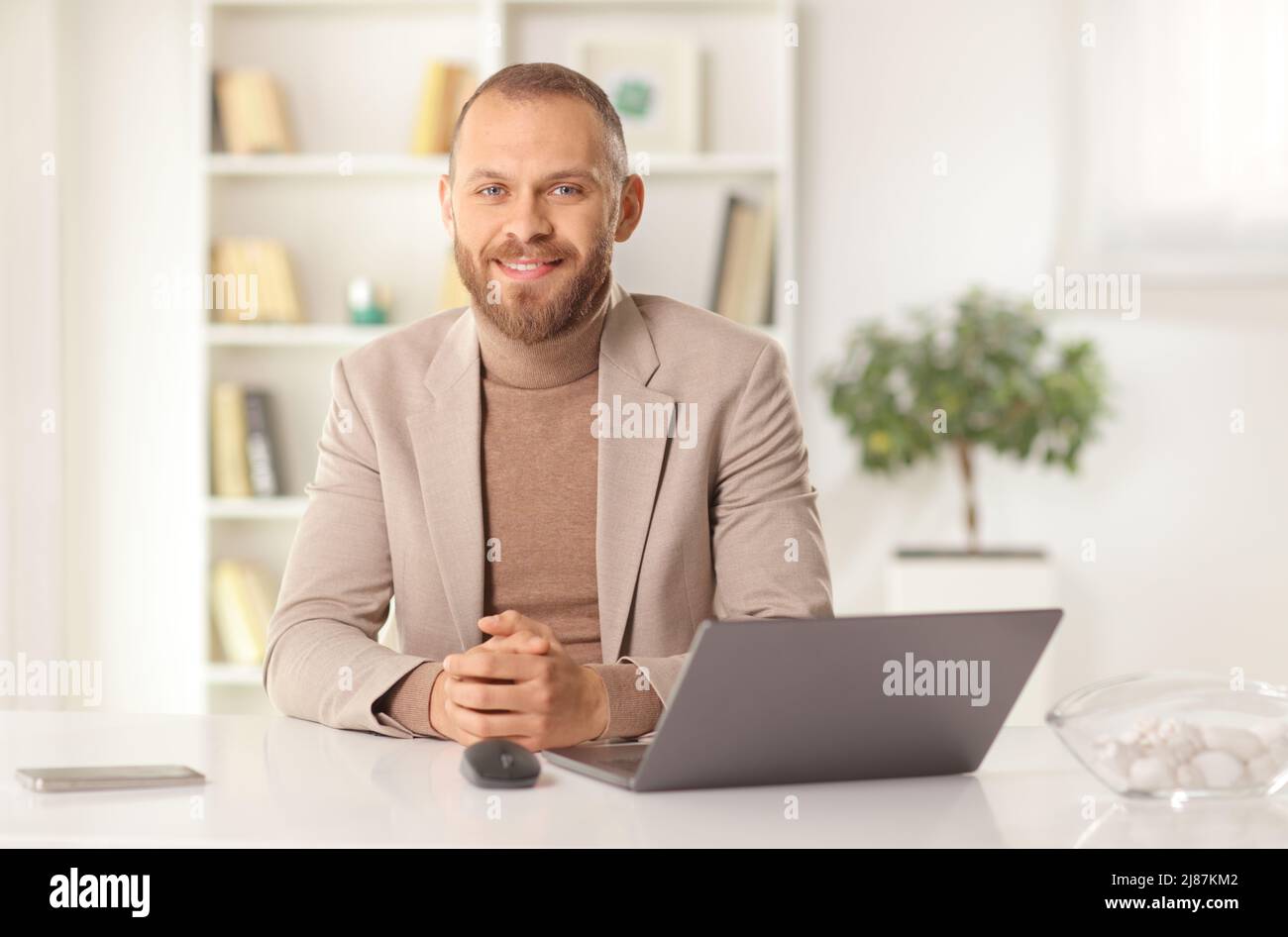 Young man sitting at table with a laptop computer and looking at camera Stock Photo