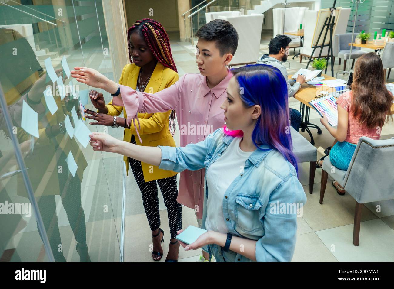 multiracial group standing near wall and put sticky sticker on glass Stock Photo