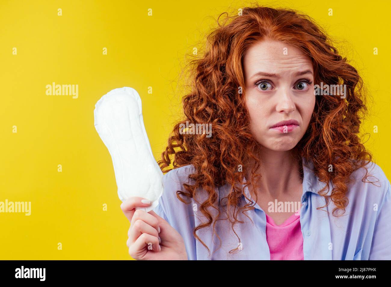 embarrassment redhaired ginger curly woman looking shyness and holding sanitary pads in studio yellow background Stock Photo