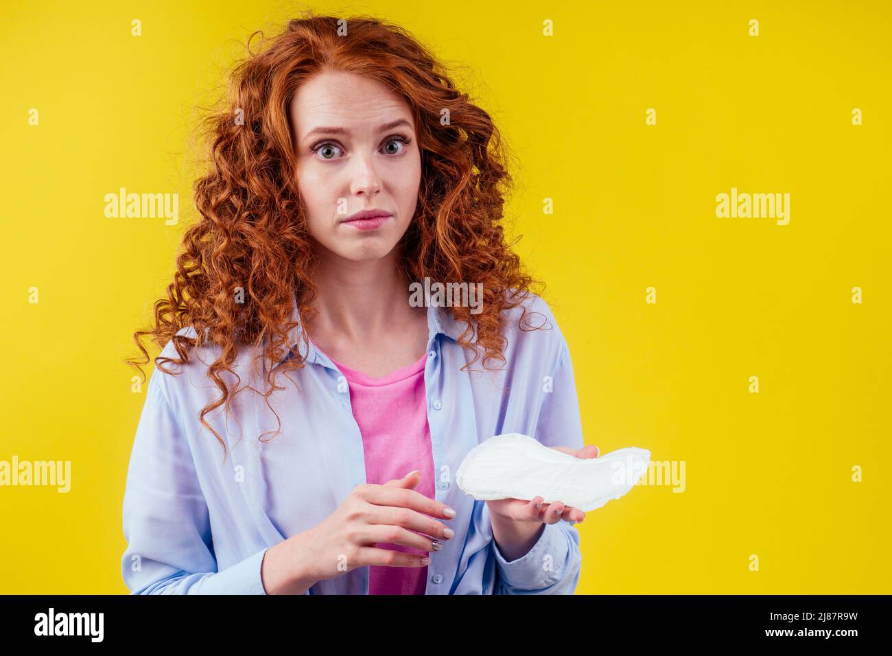 embarrassment redhaired ginger curly woman looking shyness and holding sanitary pads in studio yellow background Stock Photo