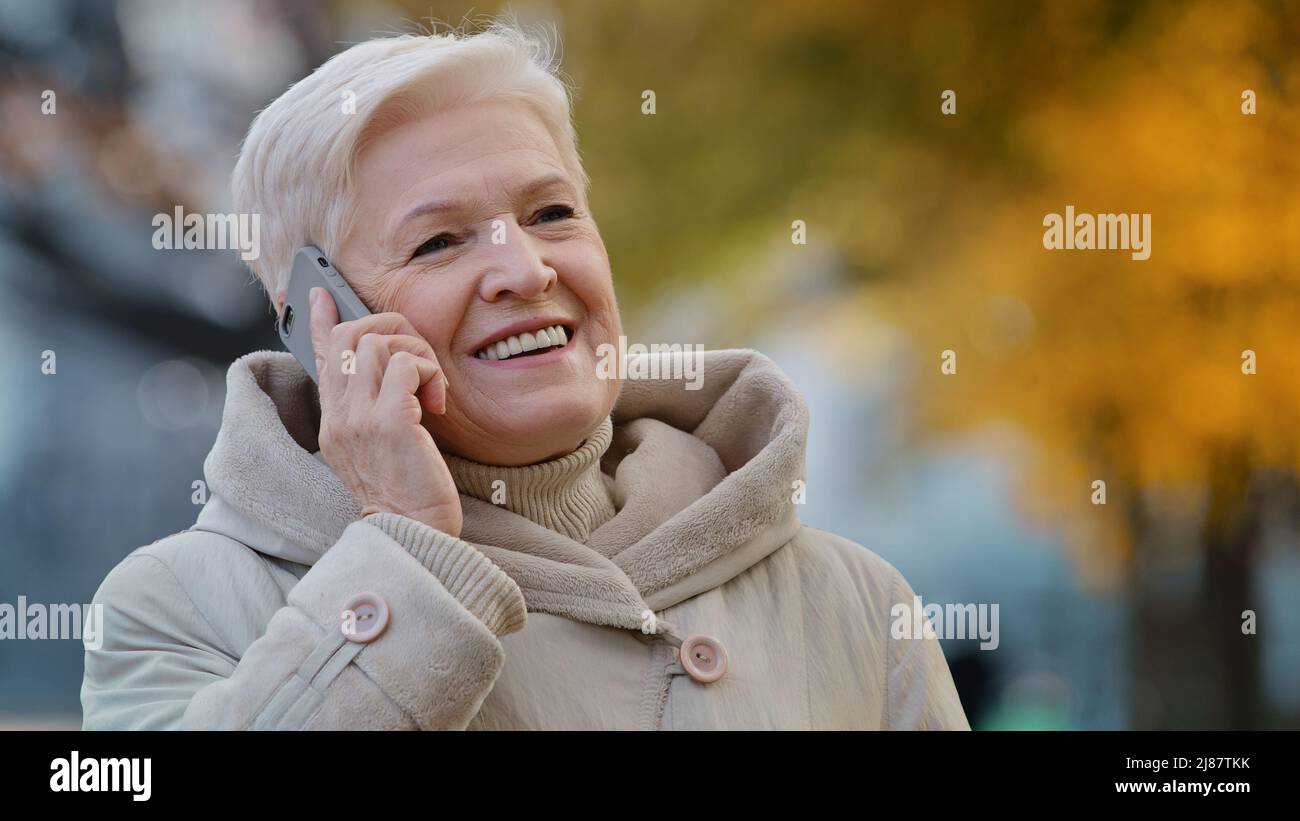 Close-up elderly lady speak on smartphone shares news grandma enjoying using device outdoors positive aged woman smiling talking with children by Stock Photo