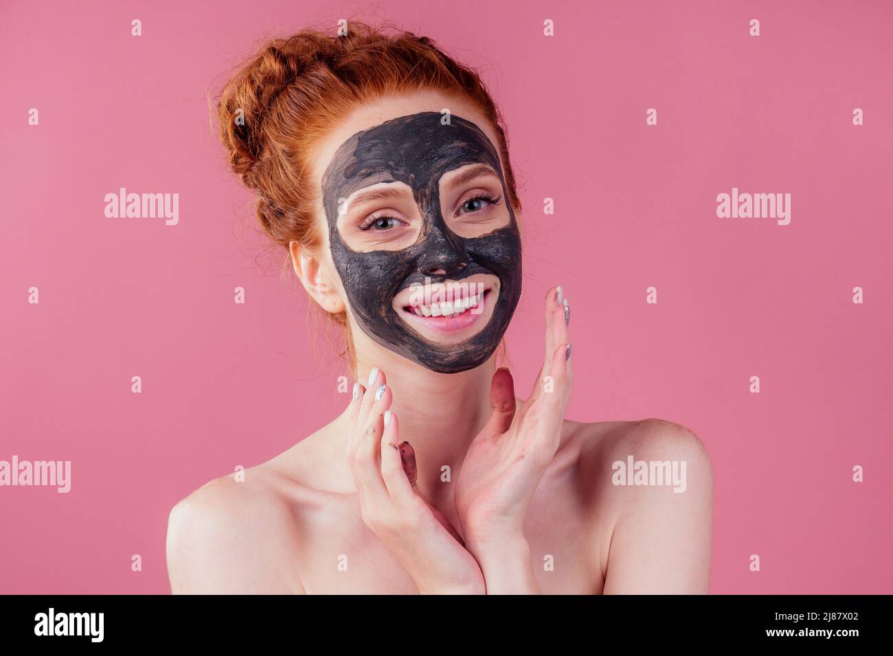 redhaired ginger young caucasian woman with natural anti acne mask on her pretty perfect face in studio pink background Stock Photo