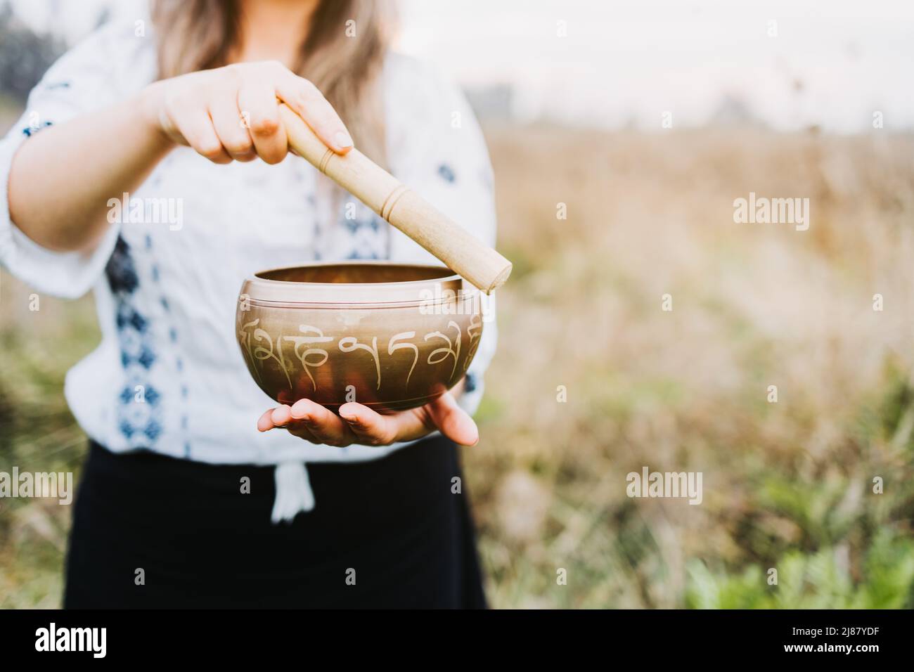 White and black dressed buddhist woman playing a tibetan singing bowl with a wooden stock. Selective focus. Stock Photo