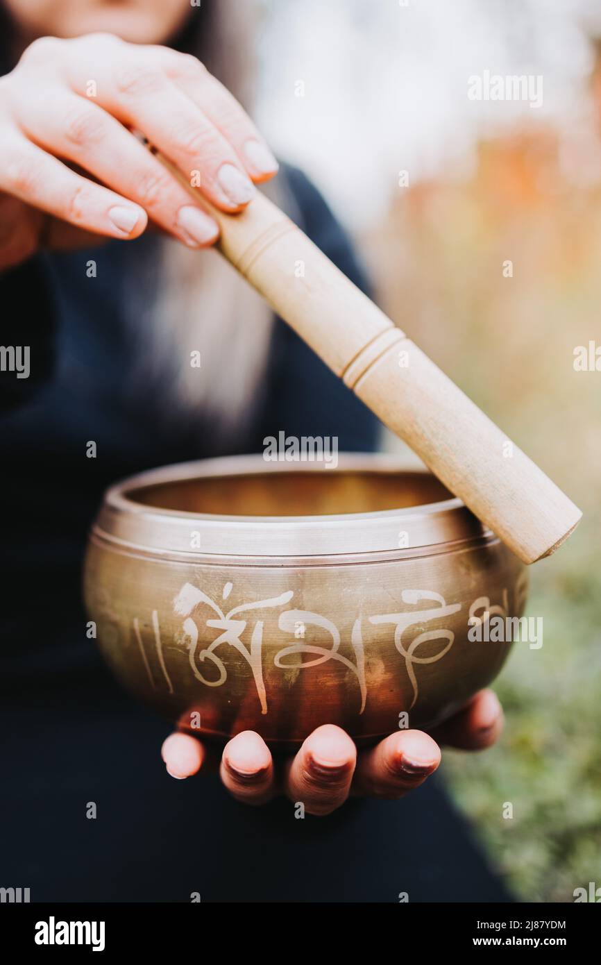 Black dressed buddhist woman holding and playing a tibetan singing bowl with a wooden stock. Selective focus Stock Photo