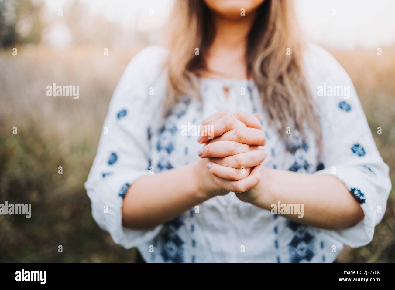 Unrecognizable woman outside praying on her knees with her hands together. Selective focus Stock Photo