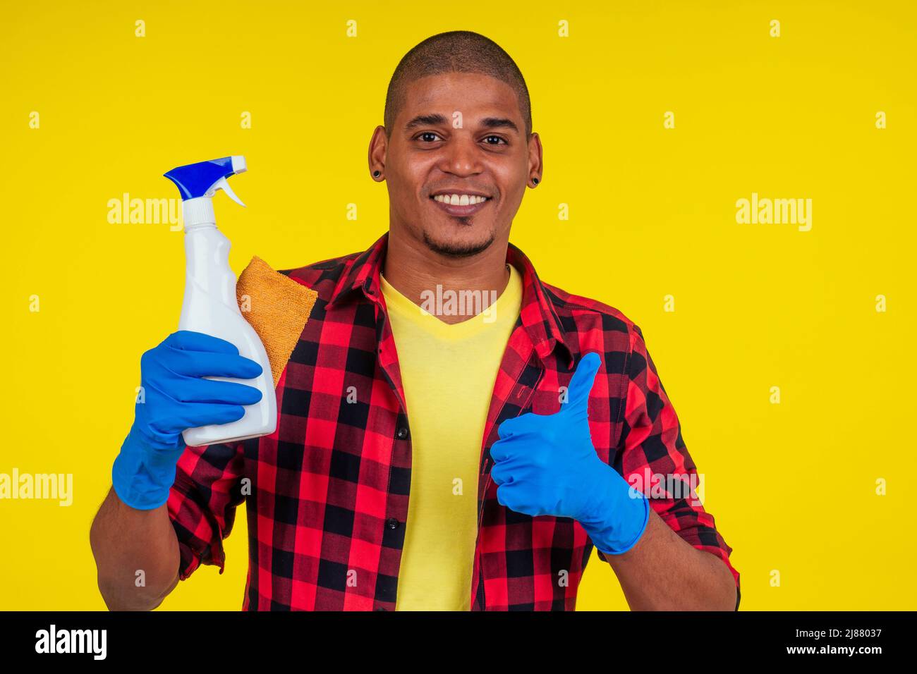 latin brazilian cleaning man wearing ribon gloves in studio yellow background Stock Photo