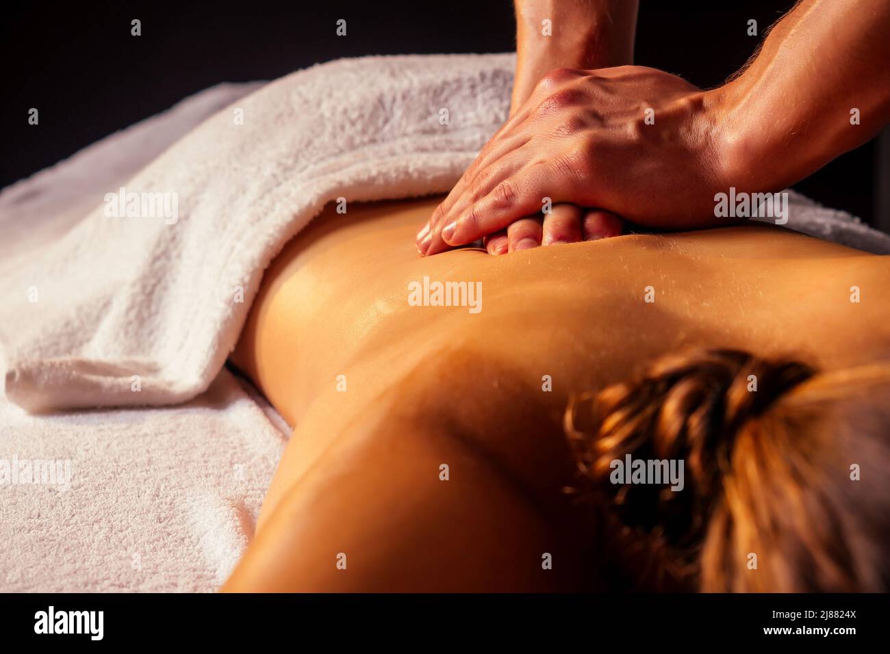 young indian woman lying on the table and getting ayurvedic massage with organic oil or honeyed in dark room.massagist male pouring out client back Stock Photo
