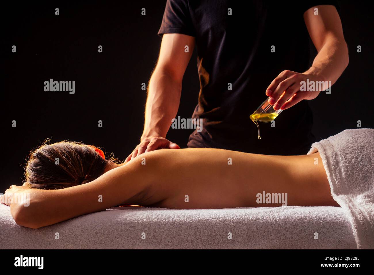 young indian woman lying on the table and getting ayurvedic massage with organic oil or honeyed in dark room.massagist male pouring out client back Stock Photo