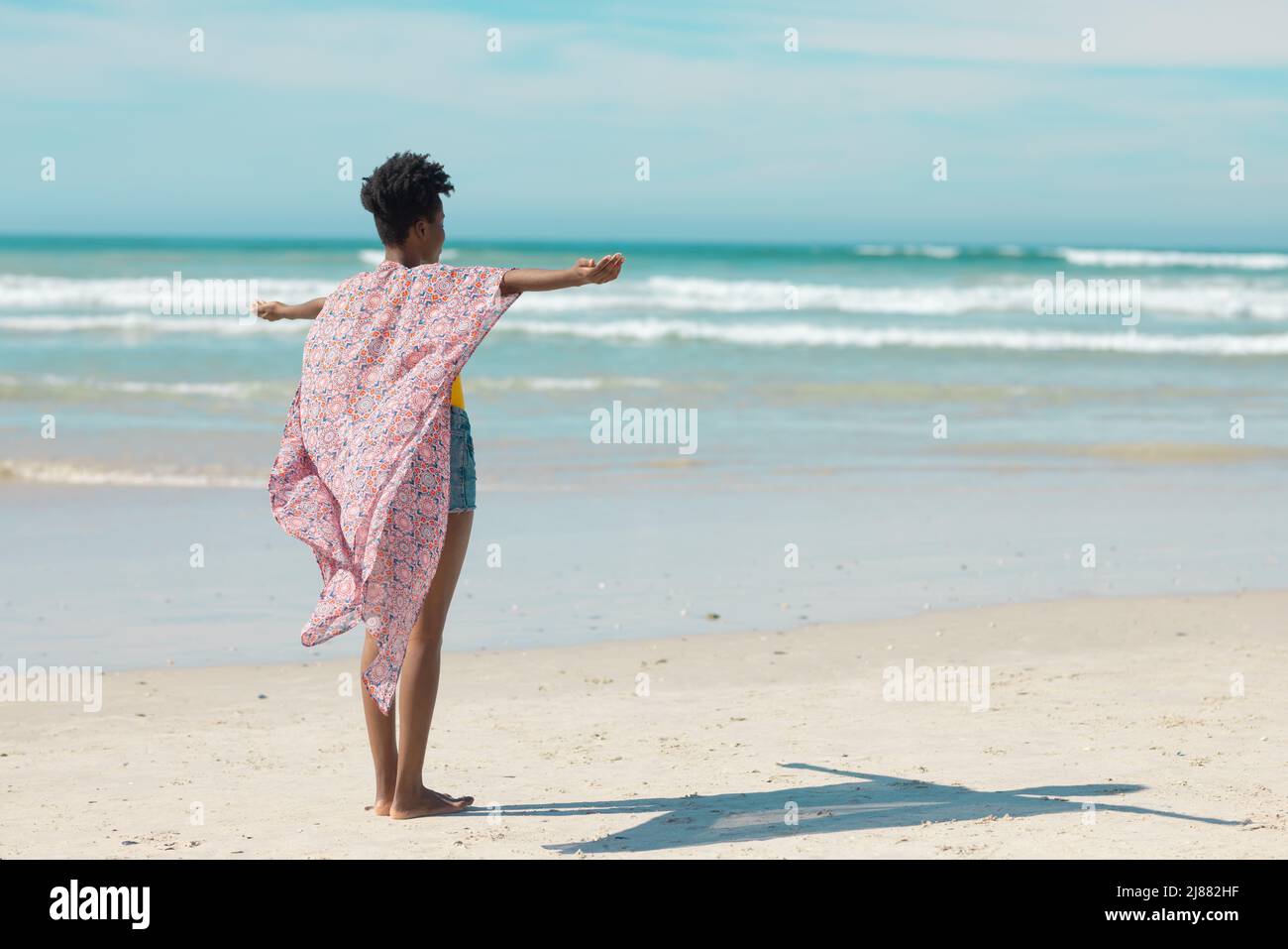 Carefree african american young woman with short hair stretching arms at beach against sky in summer Stock Photo