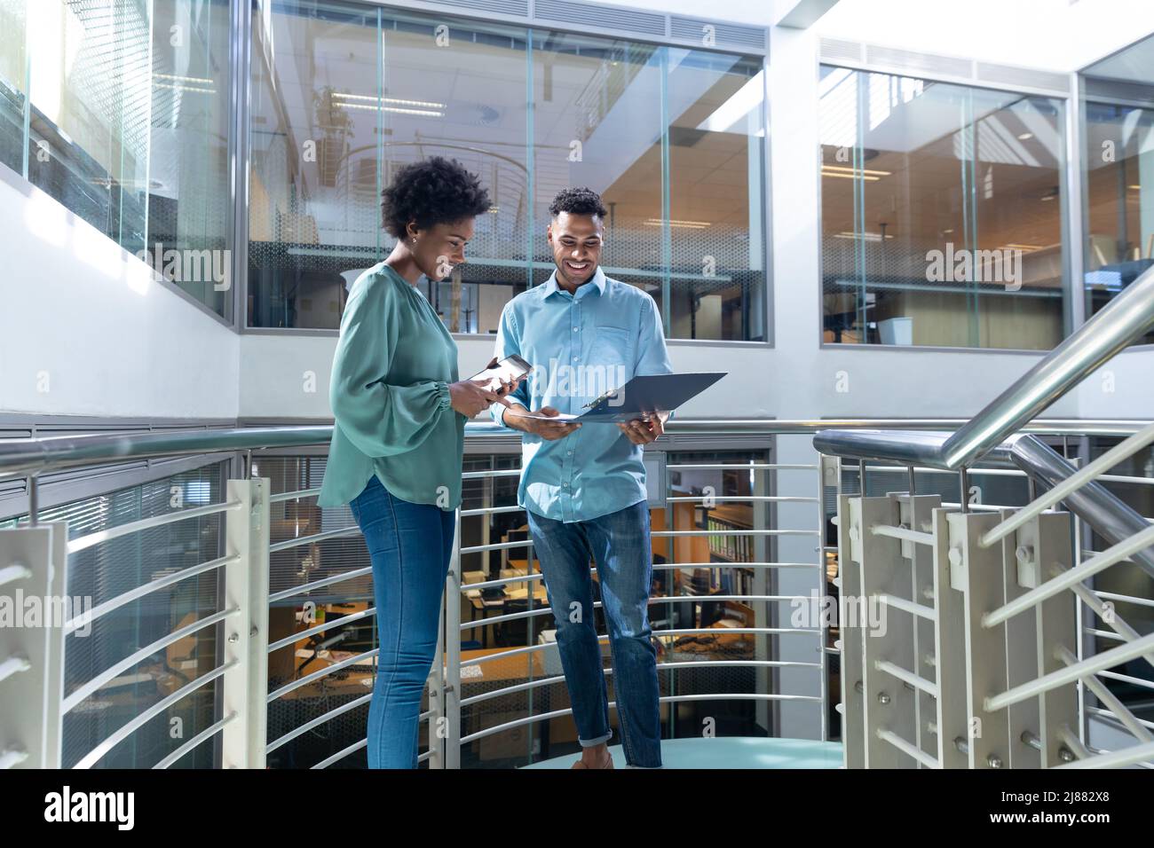 Smiling african american male and female professionals discussing over file on staircase Stock Photo