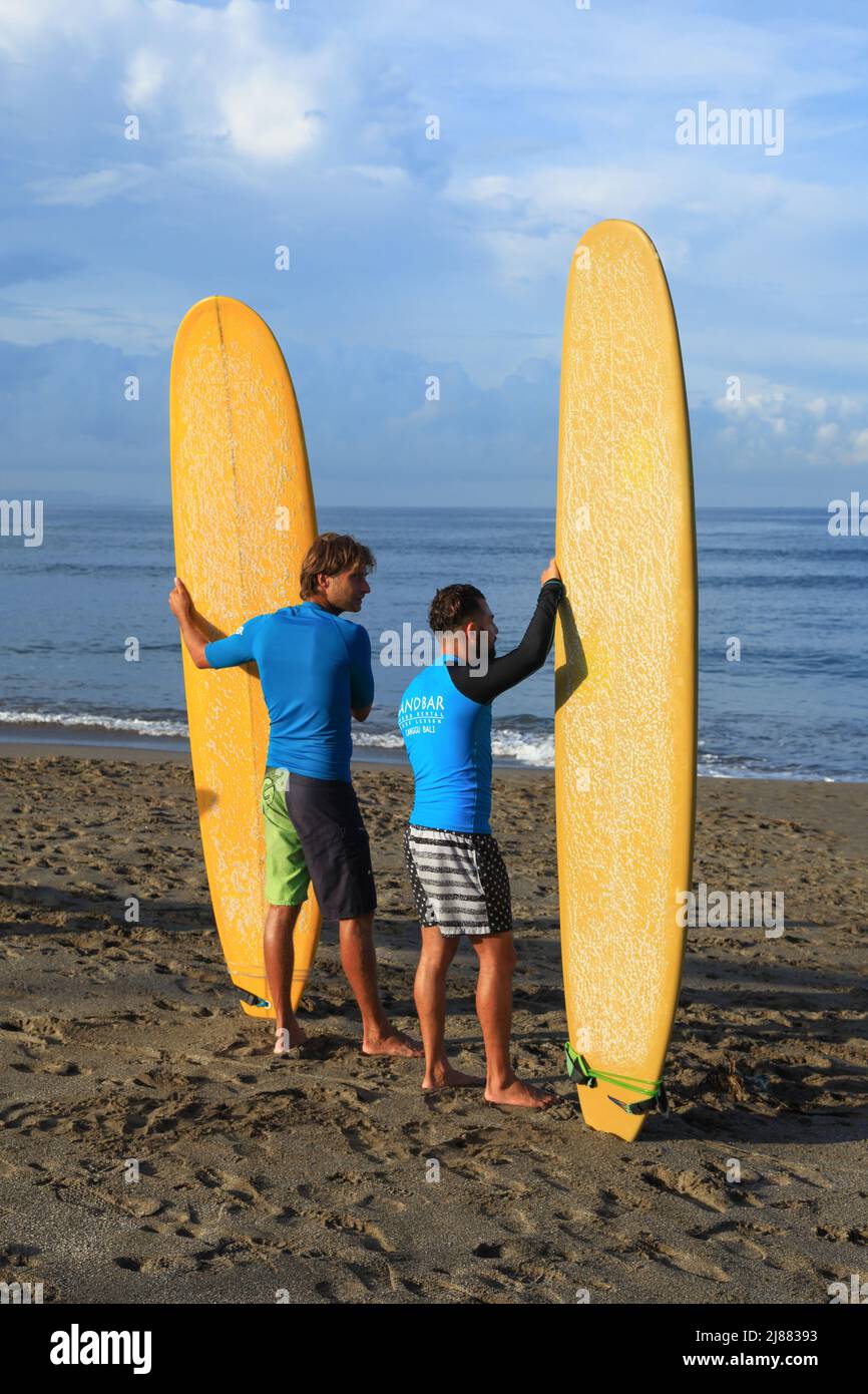 Two male Caucasian surfers standing at Batu Bolong Beach in Canggu, Bali, Indonesia carrying their long boards or malibu surfboards. Stock Photo