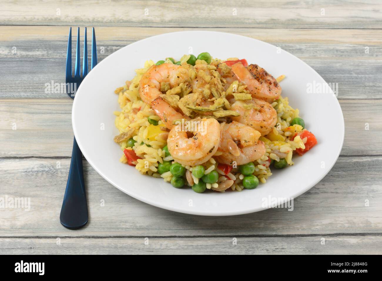 Shrimp with vegetables and white wild rice on white plate with blue fork Stock Photo