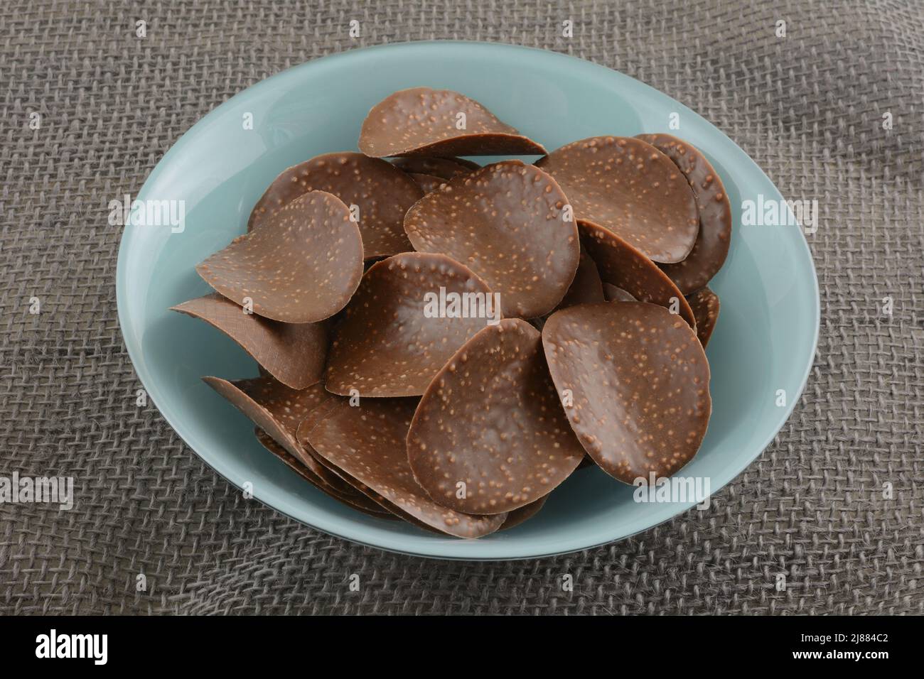 Chocolate covered chip crisps in blue snack bowl on gray burlap Stock Photo