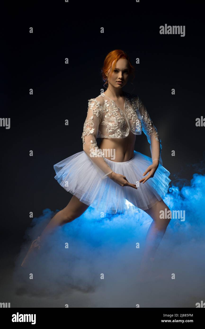 Graceful ballerina dancing in blue smoke light on stage Stock Photo