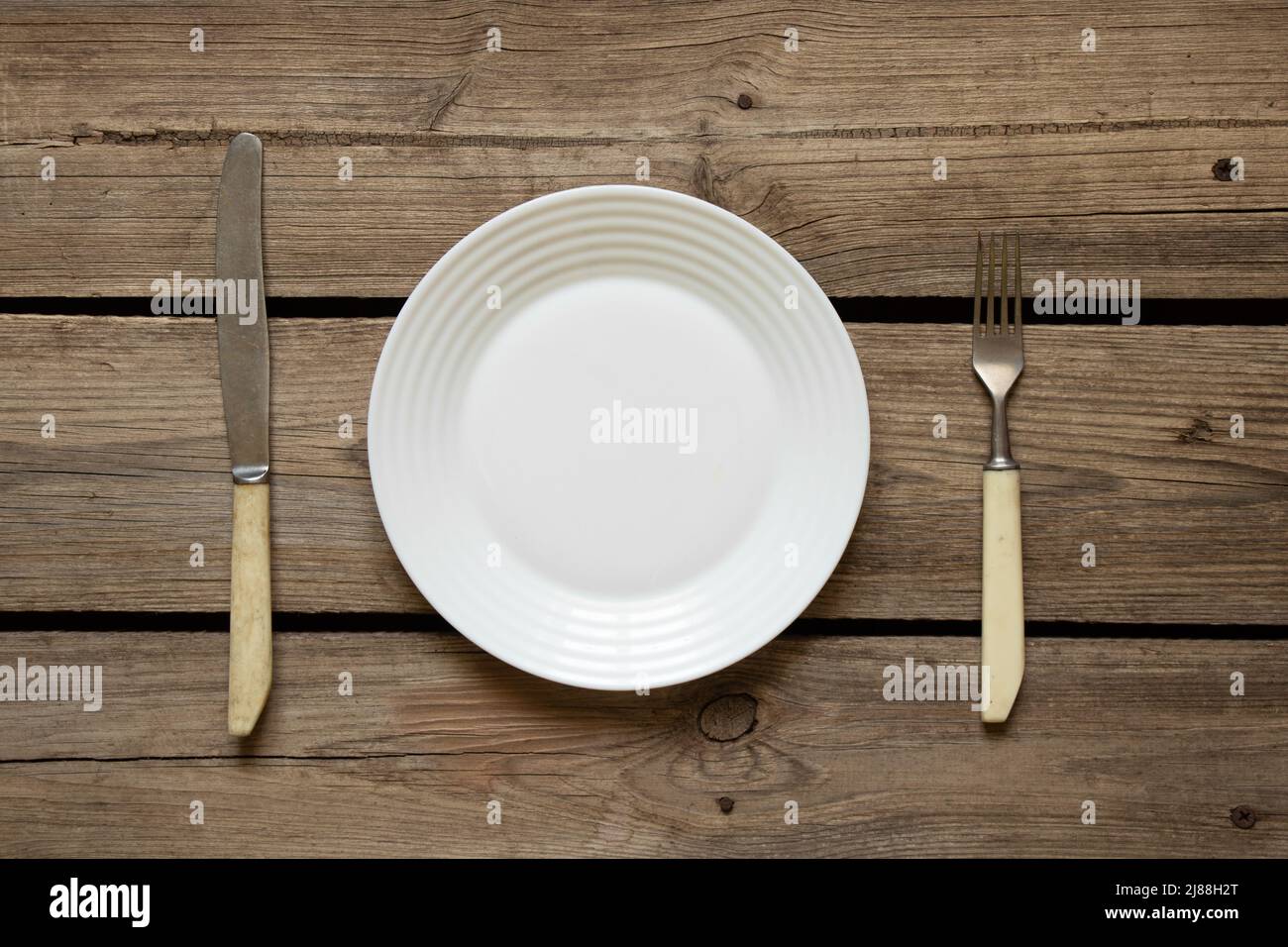 One white plate and a fork with a knife lie on an old wooden table in ...