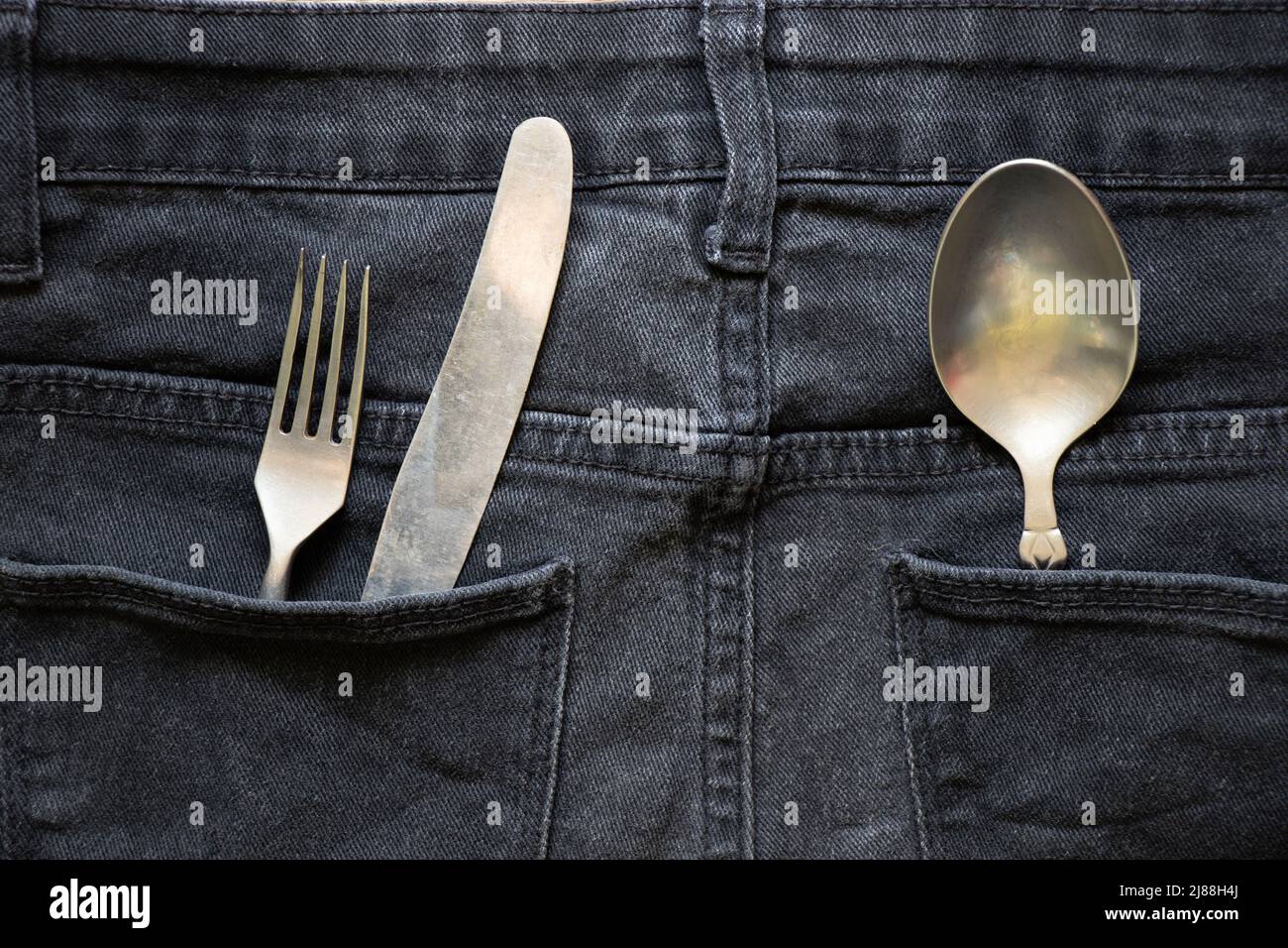 Knife, fork and spoon are in the pocket of gray jeans, cutlery in my pocket, I carry mine with me, fashion and trend, restaurant business Stock Photo
