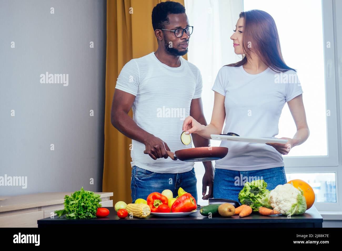 Korean woman wearimg white cotton t-shirt with her african american boyfriend cooking in fry pan bresksast Stock Photo