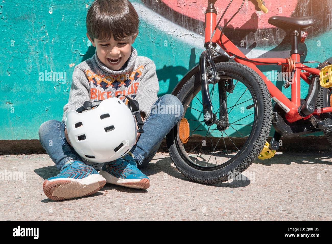 happy boy with bycicle and helmet sitted on the ground of the city Stock Photo