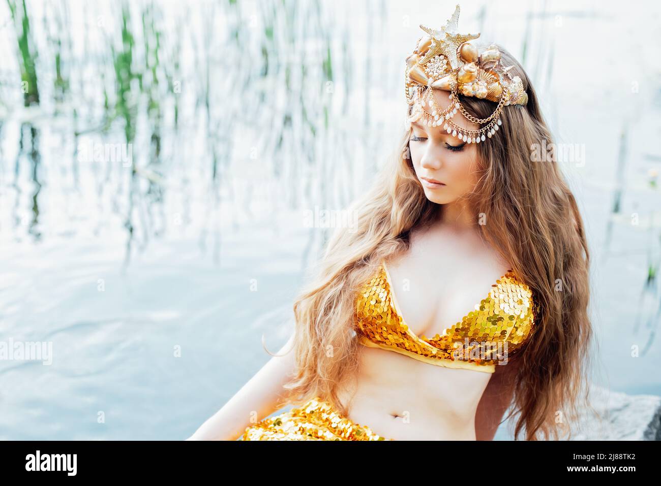 Fantasy woman real mermaid with trident myth goddess of sea with golden  tail sitting in sunset on rocks.. Gold hair crown shells pearls jewelry.  Merma Stock Photo - Alamy