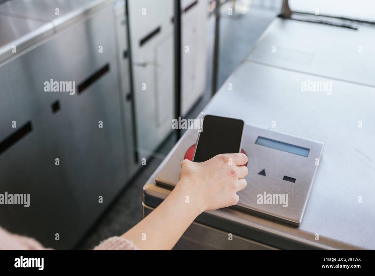 Girl passing her train ticket through the machine with her mobile phone on the station. NFC and contactless technology concept Stock Photo