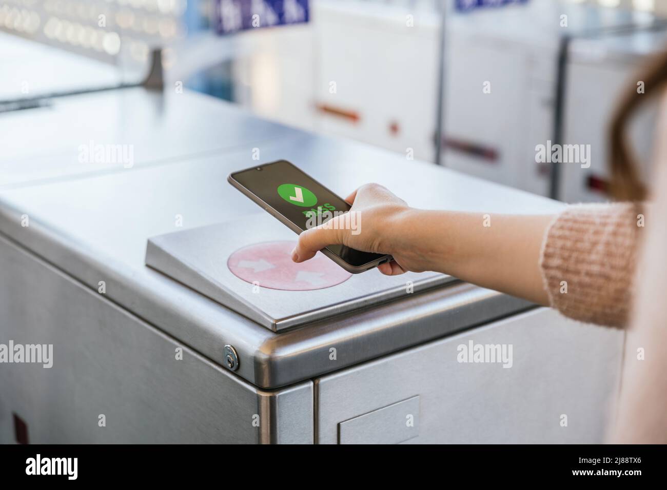 Woman's hand ticking her transport ticket in the machine with her mobile phone on train station. NFC and contactless technology concept Stock Photo
