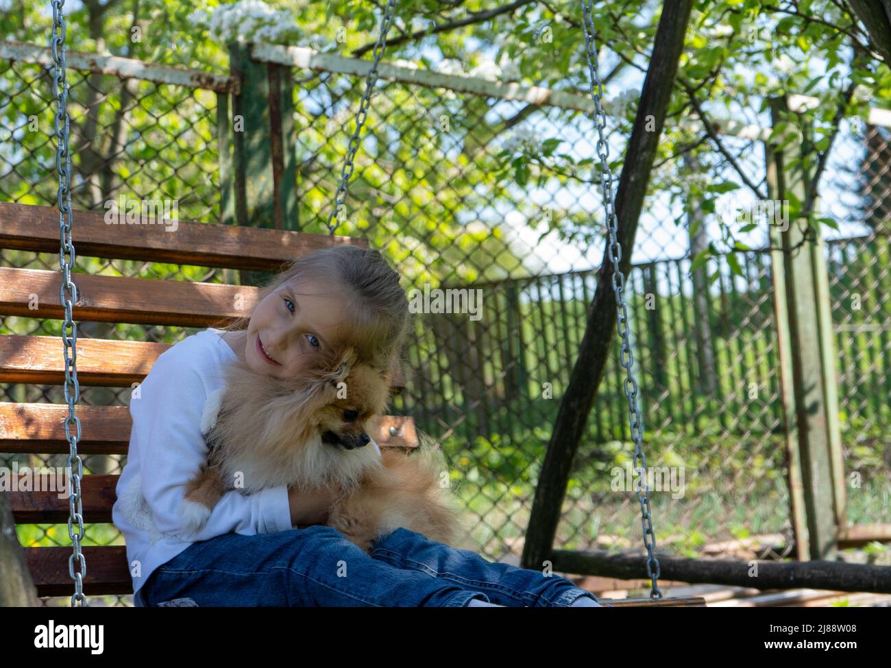 little girl hugging her dog cuddling up to her while riding on a swing on a spring day Stock Photo