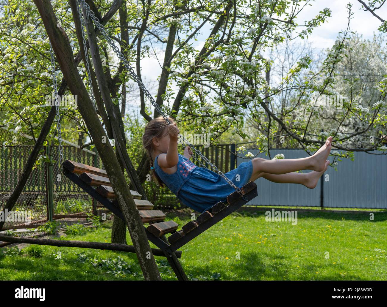 little girl barefoot rides on a swing on a sunny day Stock Photo