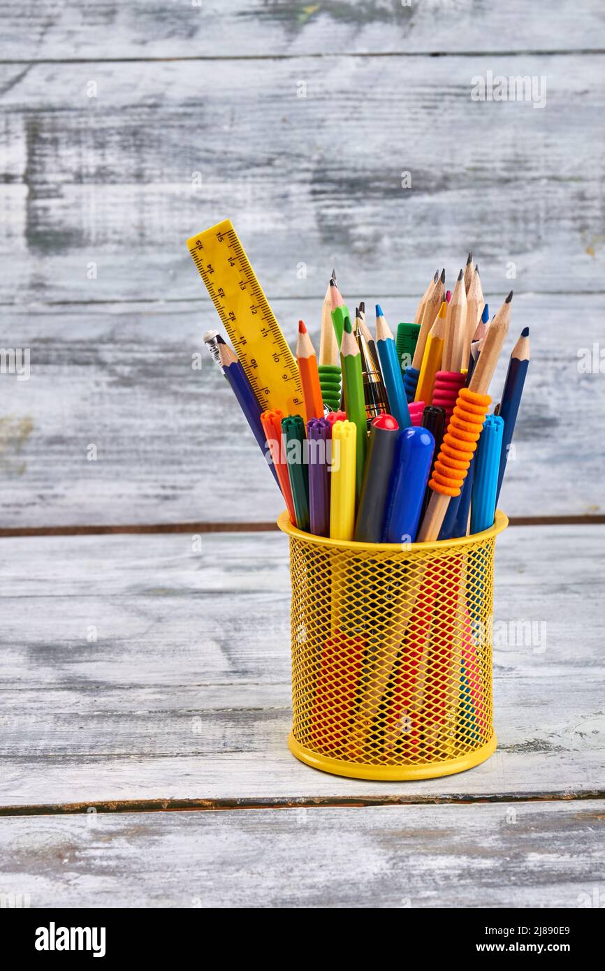 Vertical shot yellow holder with lots of pens and ruler. White wooden desk background. Stock Photo