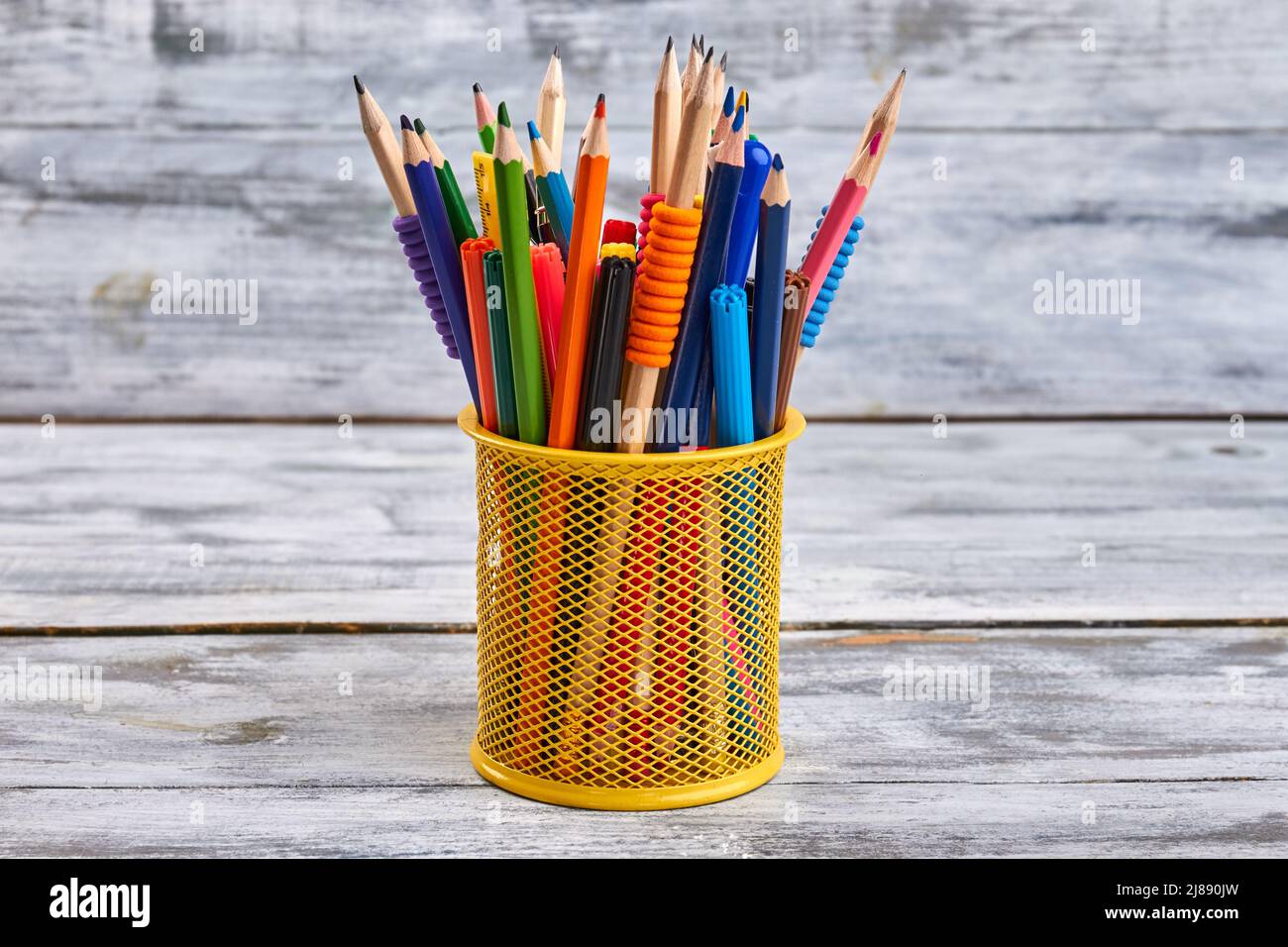 Yellow holder full of pens and pencils. White desk background. Stock Photo