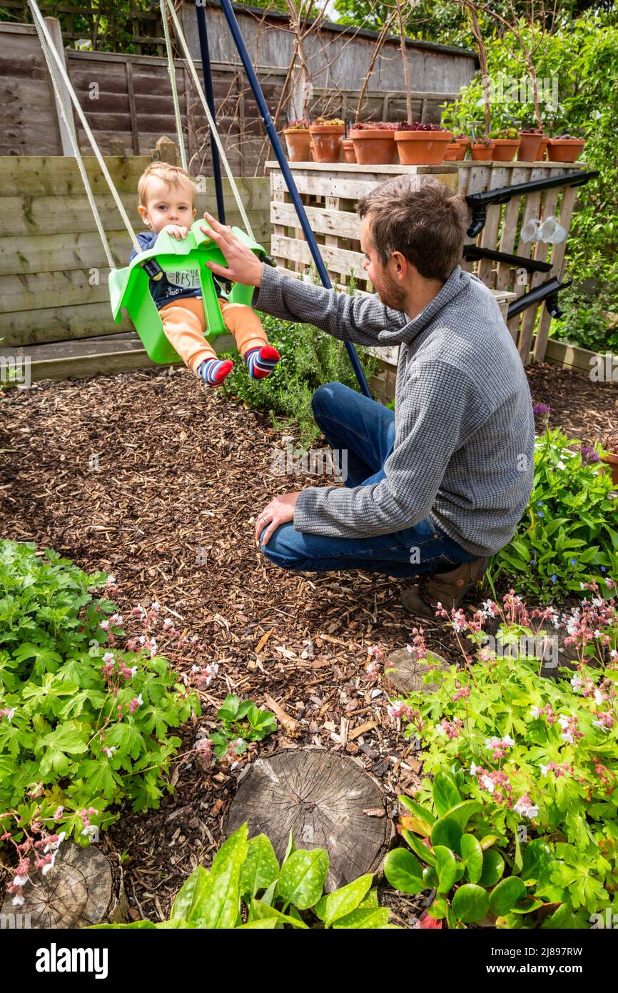 Father playing with his son on a swing in a child friendly garden, UK 2022 Stock Photo