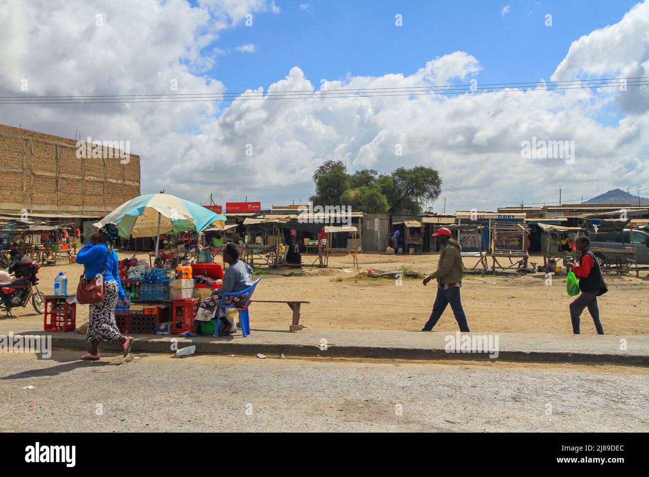 People walk by market stall in front of shops and marketplace in town in Kenya. Africa Stock Photo