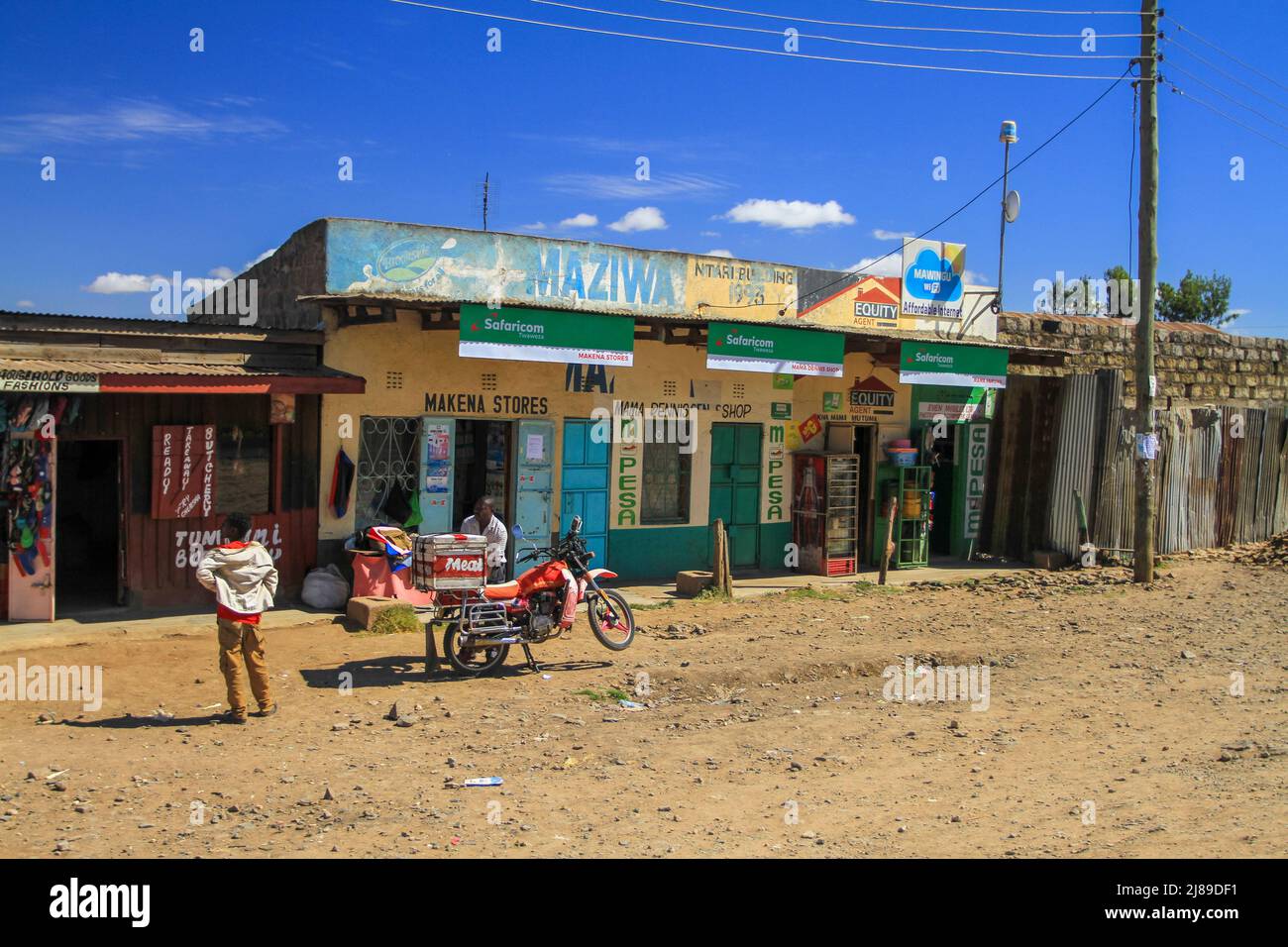 Shops in village including butcher and Safaricom mobile provider and MPesa store. Animal meat wagon with transport by motorbike. Kenya, Africa Stock Photo