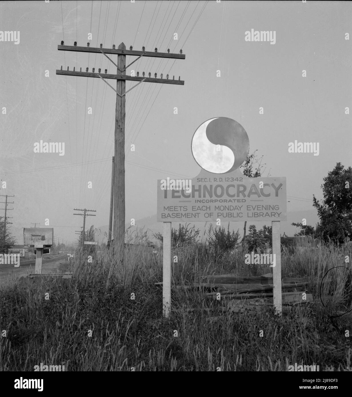 New sign, erected seven years after Howard Scott talked of a survey of North America and formation of energy units, which had widespread vogue in the early years of depression. Josephine County, Oregon. [Sign: 'Technocracy Incorporated - Meets Each Monday Evening - Basement of Public Library']. Stock Photo