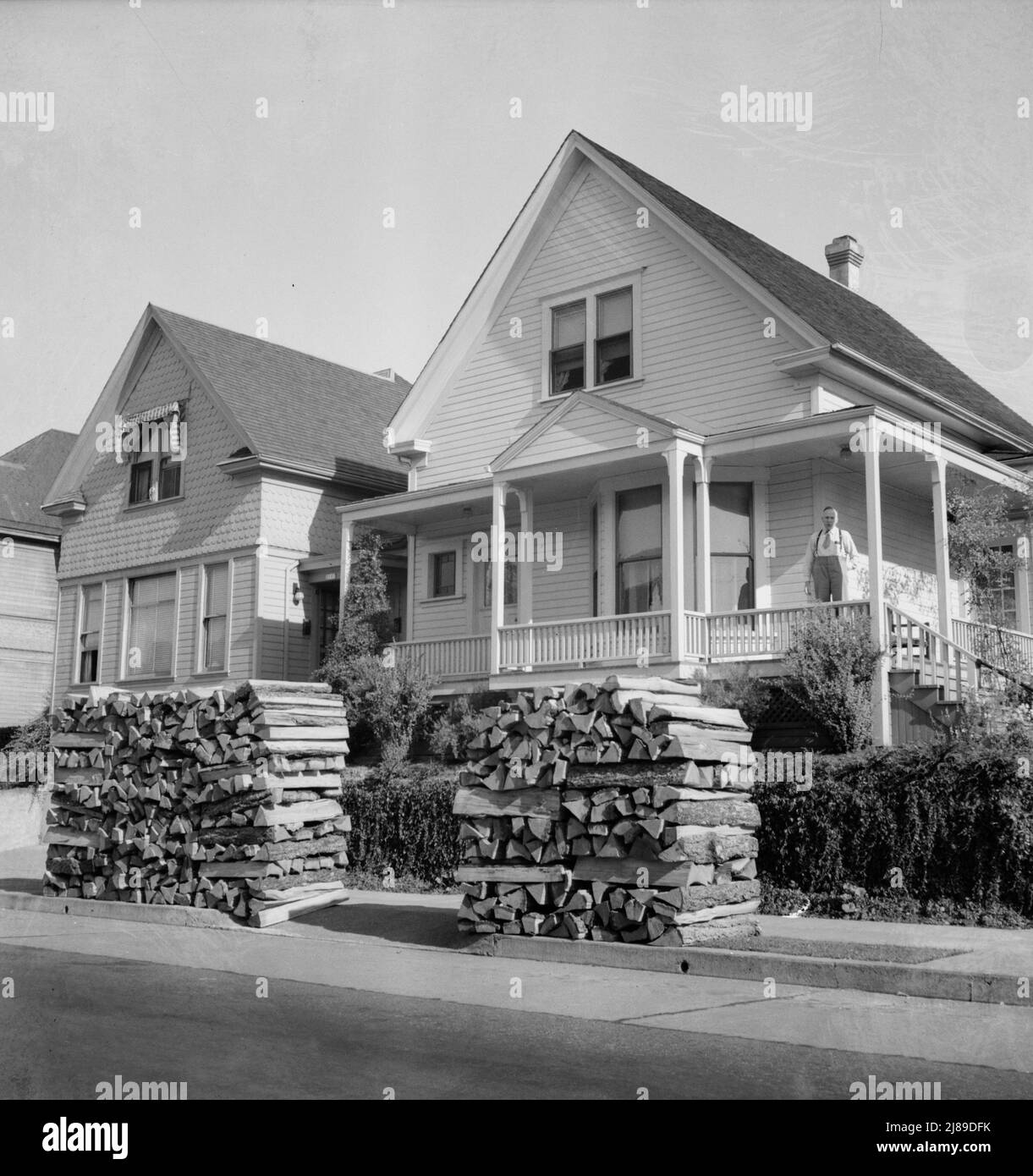 Woodpiles along the street are a characteristic of Portland, Oregon. Costs five dollars and fifty cents per cord, and must be hauled thirty-five miles. (Shows homeowner on porch.) Portland, Oregon. Stock Photo
