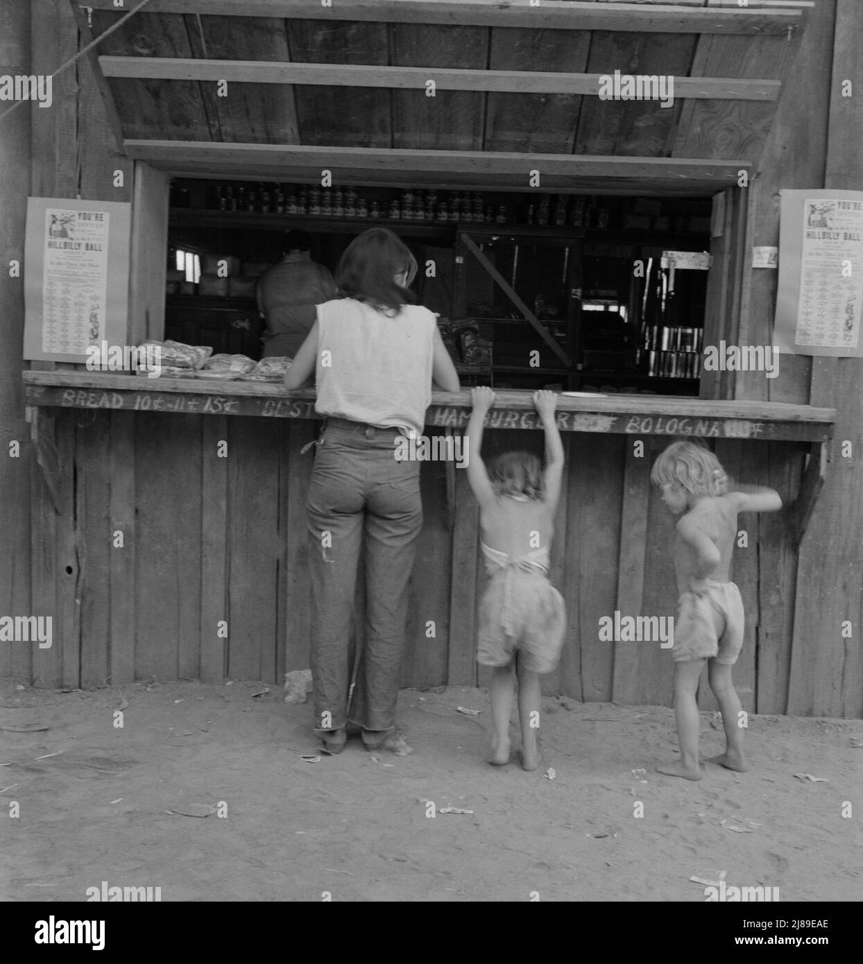 Hop picker with her children goes from paymaster's window to company-owned store adjoining. She had earned forty two cents that morning, spent it for one pound bologna sausage, one package &quot;Sensation&quot; cigarettes, one &quot;mother's cake.&quot; Oregon, Josephine County, near Grants Pass. Stock Photo