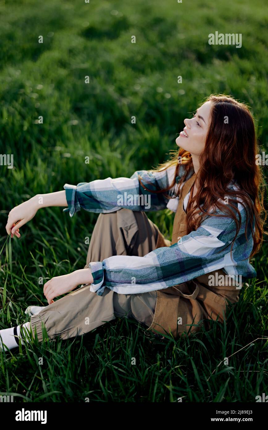 A young, beautiful woman lounges on the green grass in the park wearing