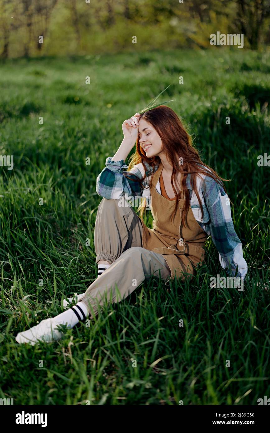 A young, beautiful woman lounges on the green grass in the park wearing