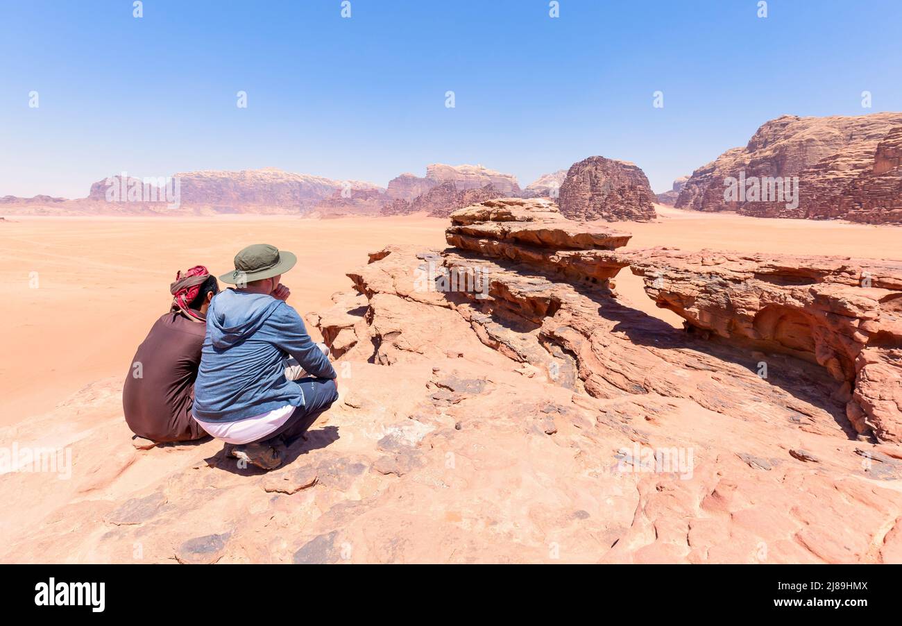 one tourist with his local guide looking at the stone arch in the desert of wadi rum in Jordan. Blue sky Stock Photo