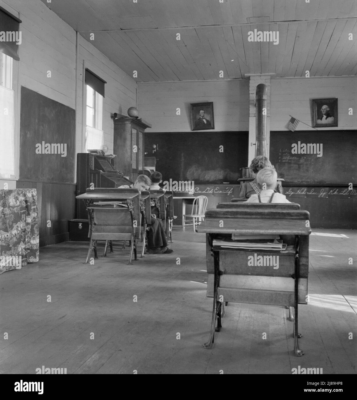 9:00 a.m. Four pupils attend this day, of the seven who are enrolled at the eastern Oregon county school. Between Pleasant Valley and Durkee, Baker County, Oregon. [Note stove for heating, and portraits of George Washington and Abraham Lincoln]. Stock Photo