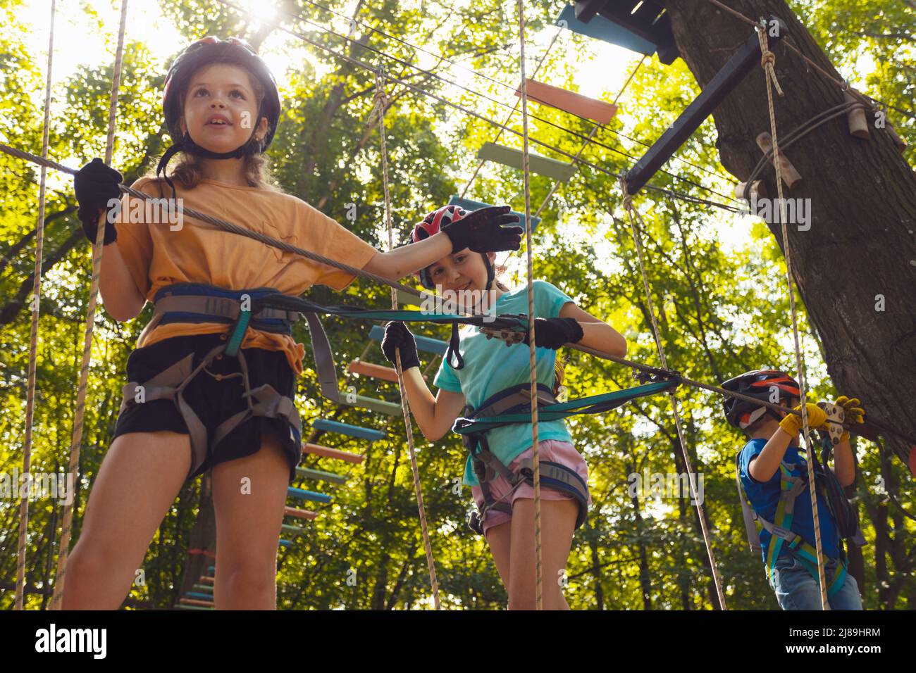 The little children in protective helmets step on the suspension bridge and hold on to the ropes Stock Photo