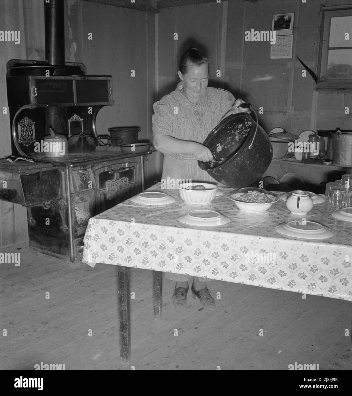 Mrs. Wardlow getting dinner after church in her basement dugout home. Dead Ox Flat, Malheur County, Oregon. [Note plates upside down to prevent contamination by flies]. Stock Photo