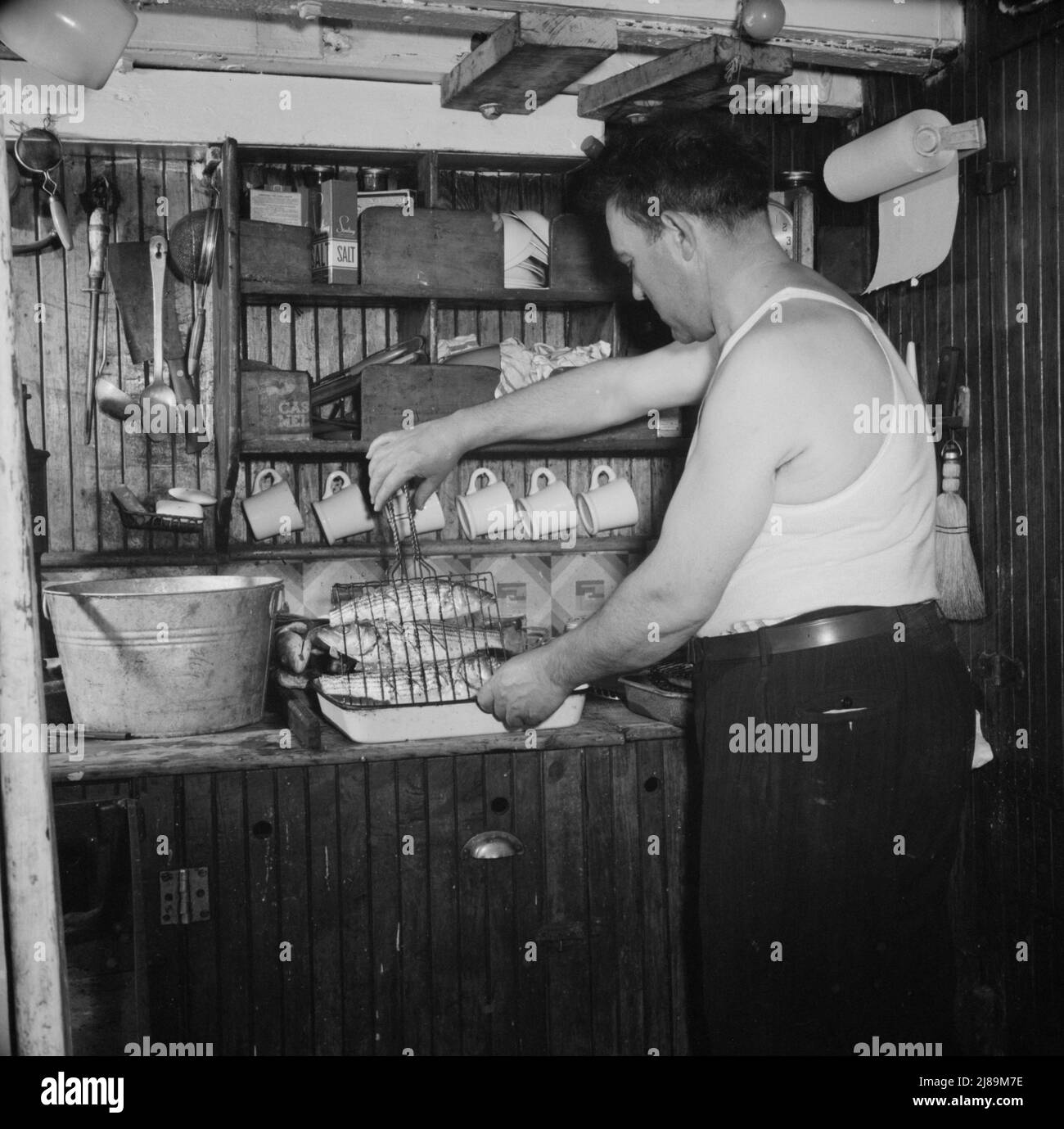 On board the Alden out of Gloucester, Massachusetts. Men lashing the seining boat to the side of the big ship, while another pumps all the water from the boat floor. This finished, they were ready to start for home with a catch of 70,000 pounds of mackerel. Stock Photo