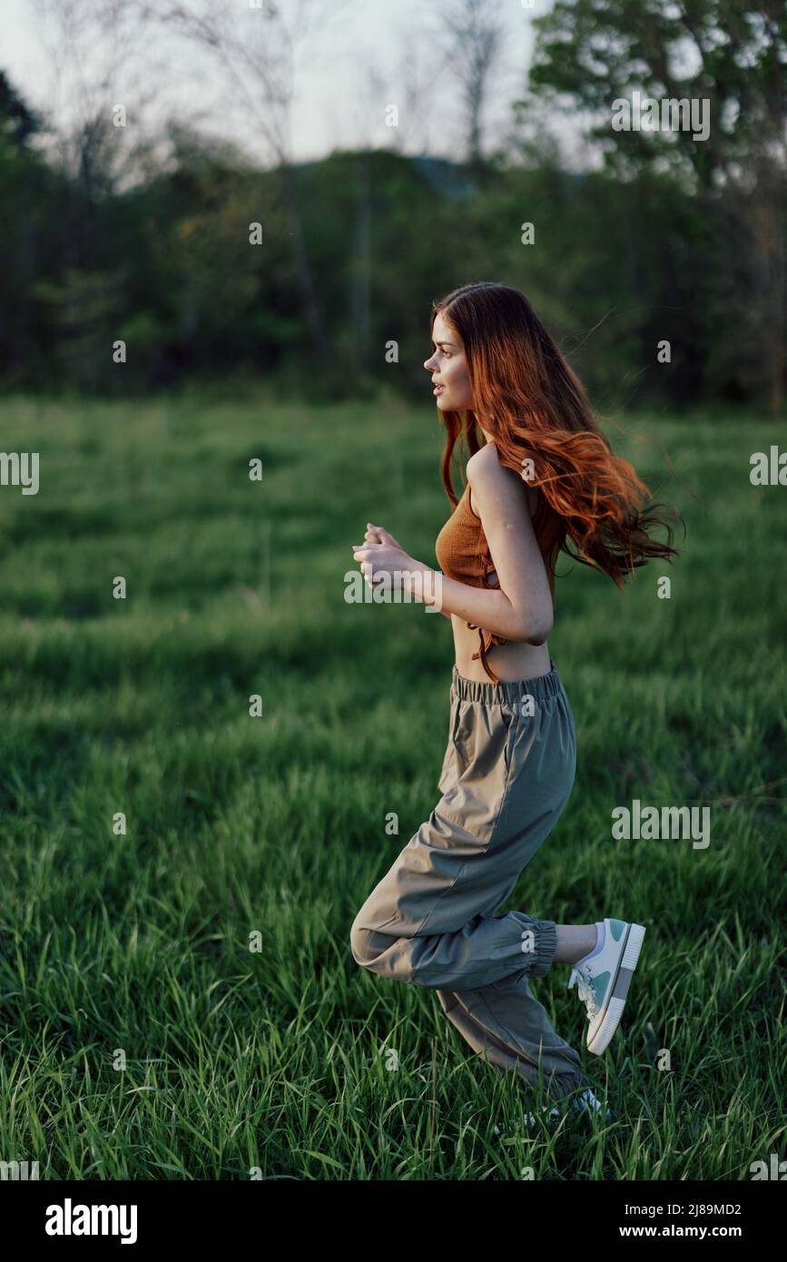 A young woman exercising outside and running in the park. in the evening on the green grass into the sunset Stock Photo