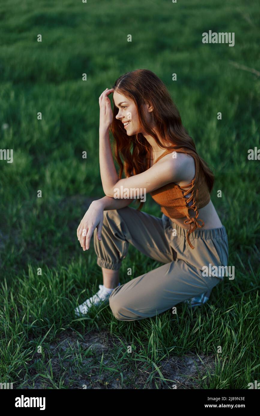 An athletic young woman warming up in the park on the green grass before an outdoor sports workout in the evening Stock Photo